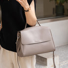 Beige handbag held by a person wearing a black sweater and beige pants.