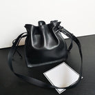 Black leather bucket bag on a black surface with a white card underneath