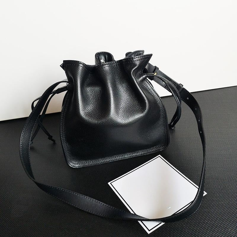 Black leather bucket bag on a black surface with a white card underneath