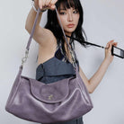 Woman holding a purple handbag against a plain background