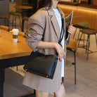 Woman in a cafe holding a black handbag and reading a newspaper.