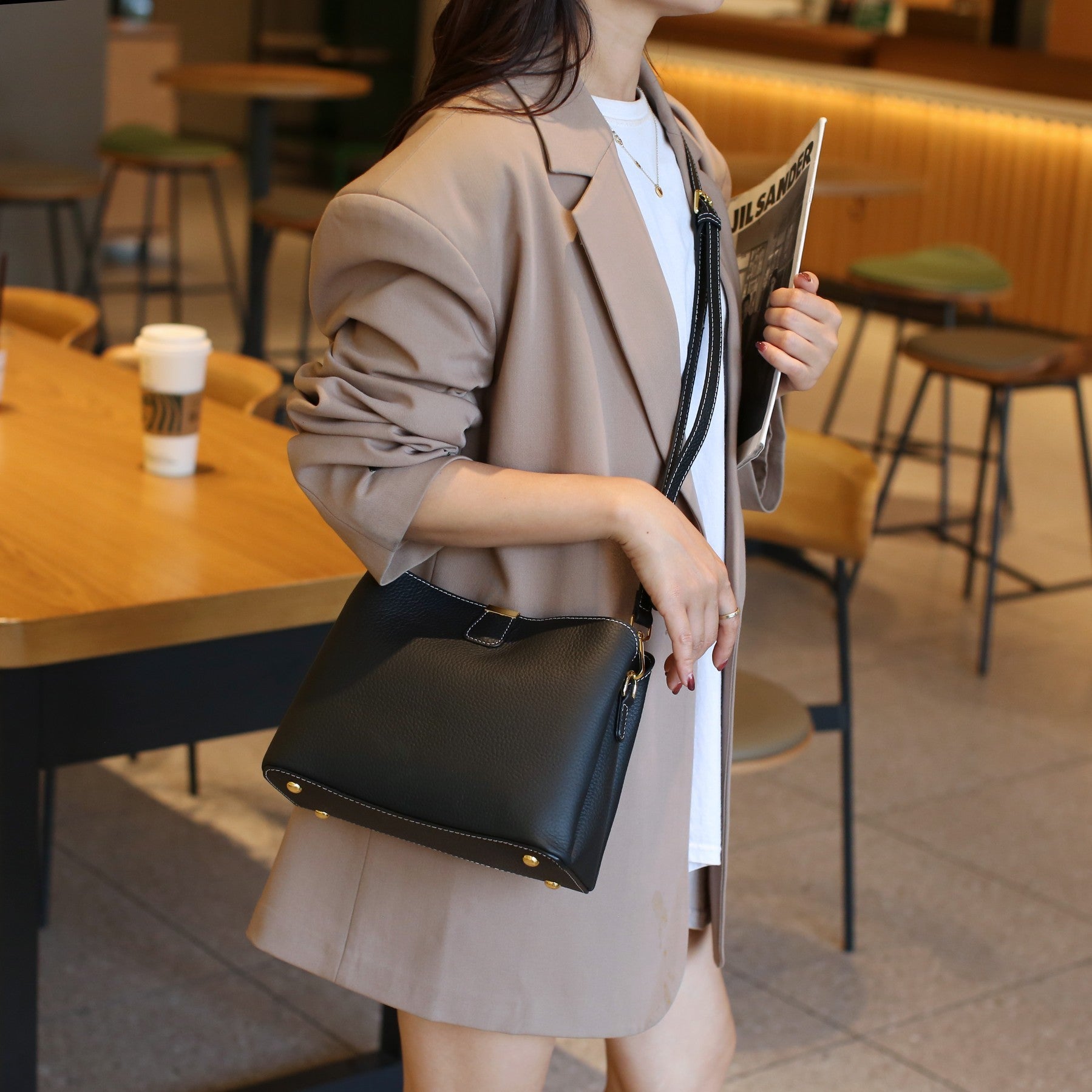 Woman in a cafe holding a black handbag and reading a newspaper.