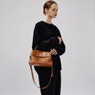 Woman holding a brown leather handbag against a plain background