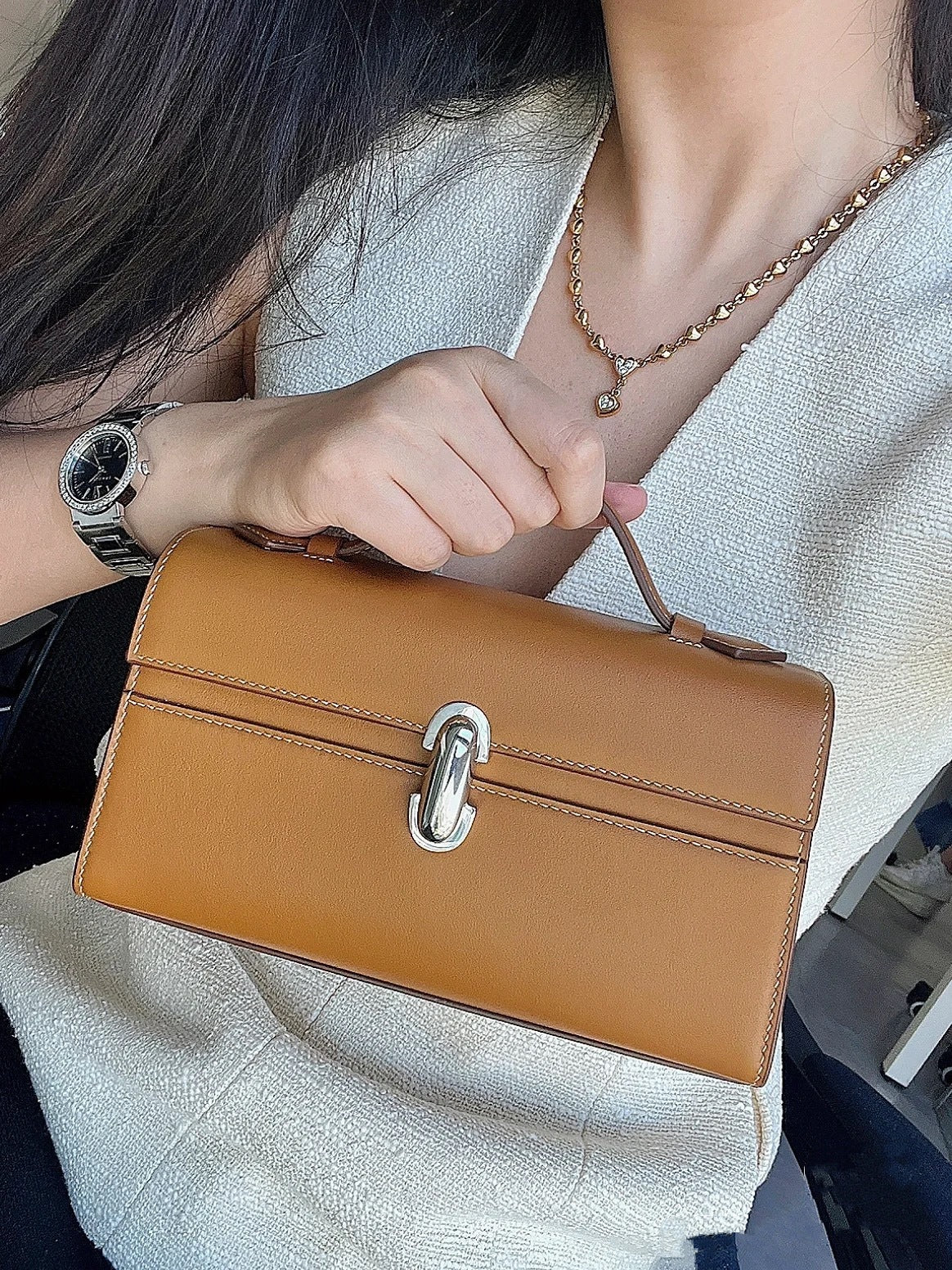 Person holding a brown handbag with a silver clasp