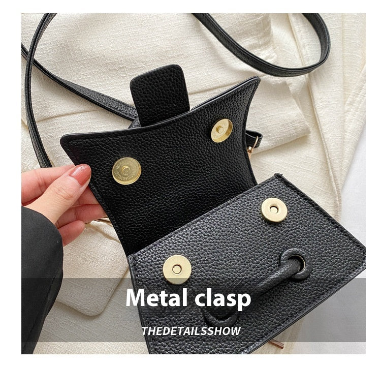 Black leather pouch with metal clasps held by a hand on a light background