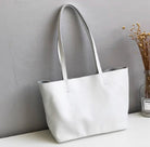 White handbag on a white surface with a gray wall and plant in the background