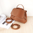 Brown leather handbag with detachable strap on a light wooden surface.