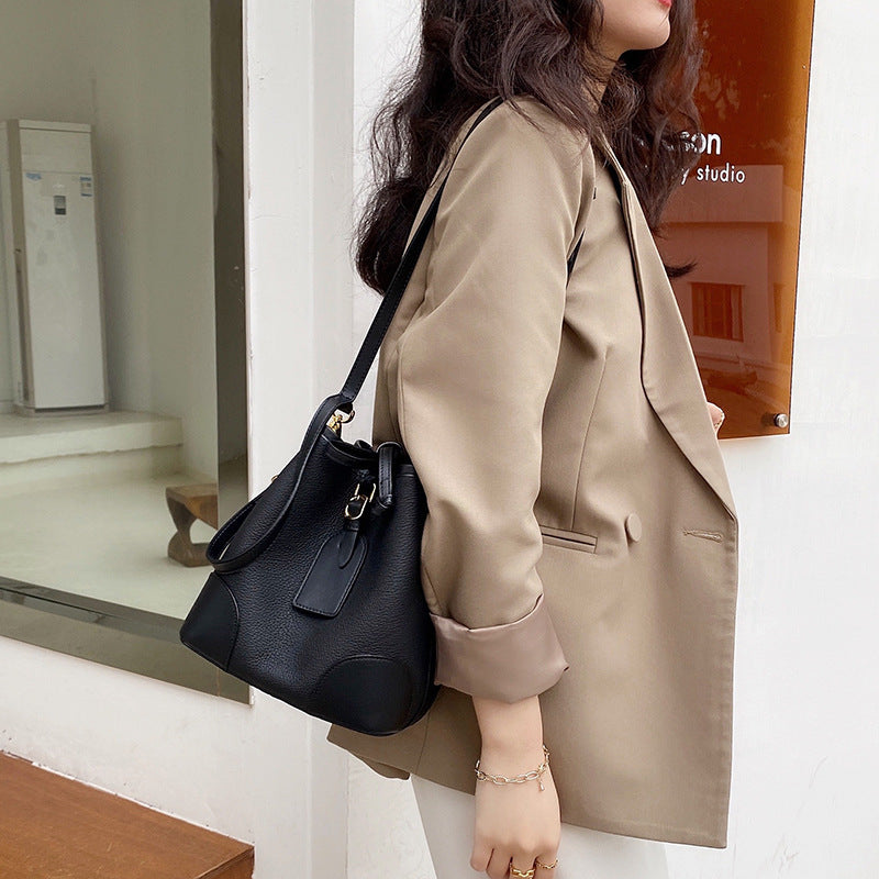 Woman in a beige coat holding a black handbag in an indoor setting