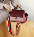 Burgundy and pink handbag with a colorful strap on a wooden surface