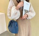 Person holding a magazine next to a blue woven bag against a beige wall.