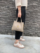 Person holding a beige handbag against a stone wall.
