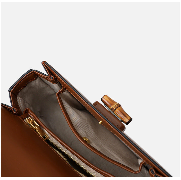 Close-up of a brown leather handbag with gold zipper and clasp on a white background
