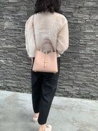 Person wearing a beige top and black pants with a pink handbag against a stone wall.