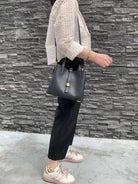 Person holding a black handbag against a stone wall background
