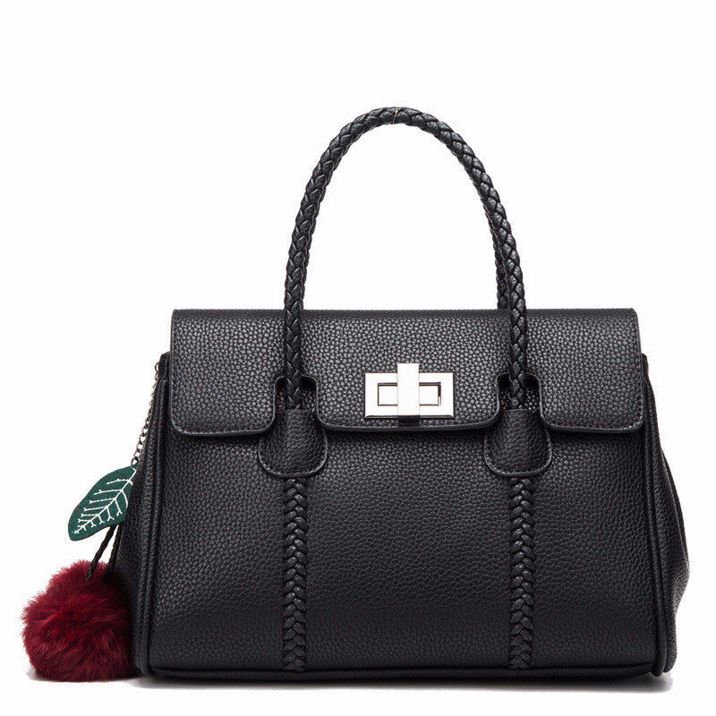 Black handbag with braided handle and decorative leaf tag on a white background