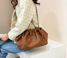 Person holding a brown woven handbag against a neutral background