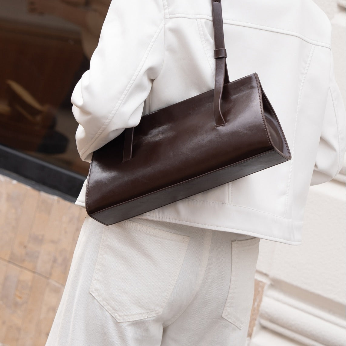 Brown leather bag held by a person wearing a light-colored outfit.