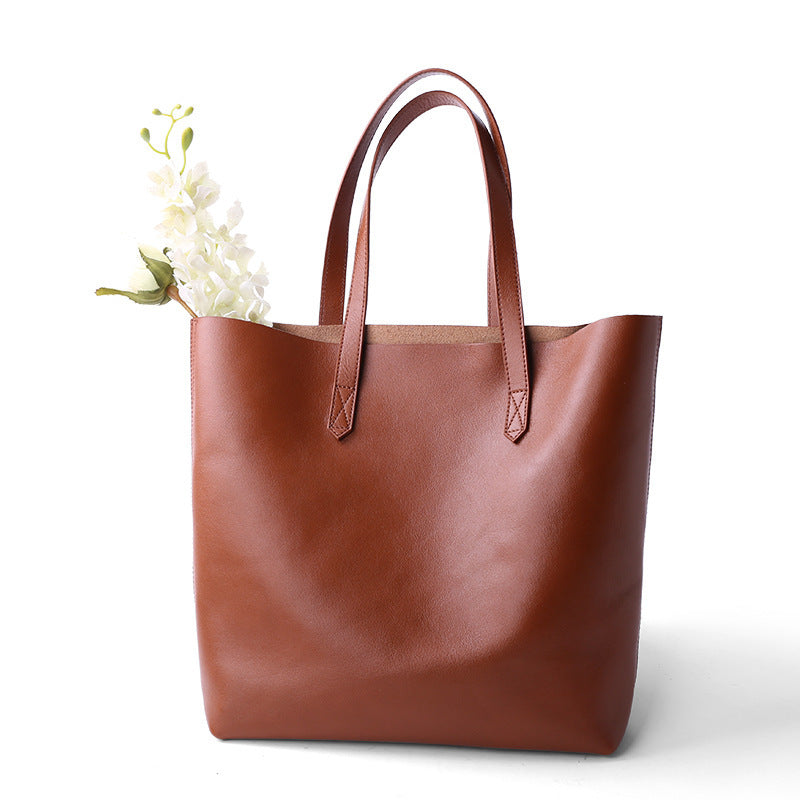 Brown leather tote bag with a floral arrangement on a white background
