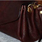 Close-up of a brown leather handbag with gold hardware on a surface with text.