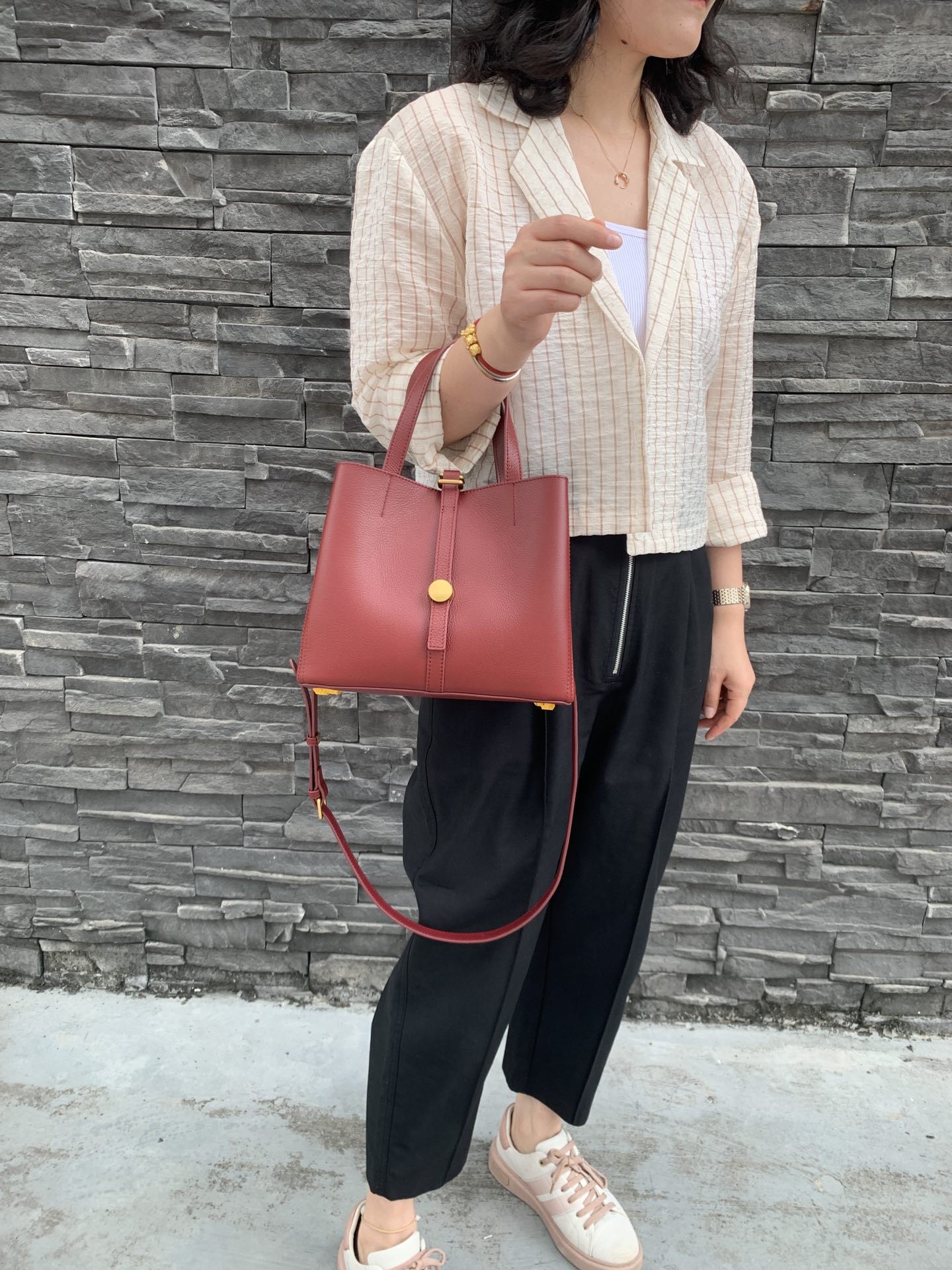 Person holding a red handbag against a stone wall background