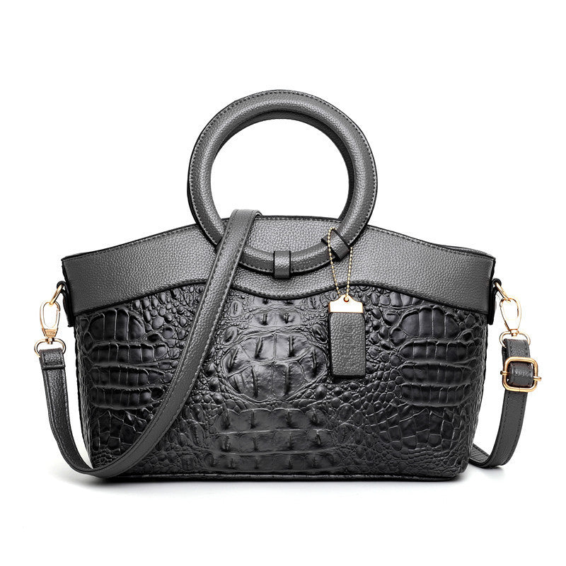 Black handbag with crocodile texture and round handle on a white background