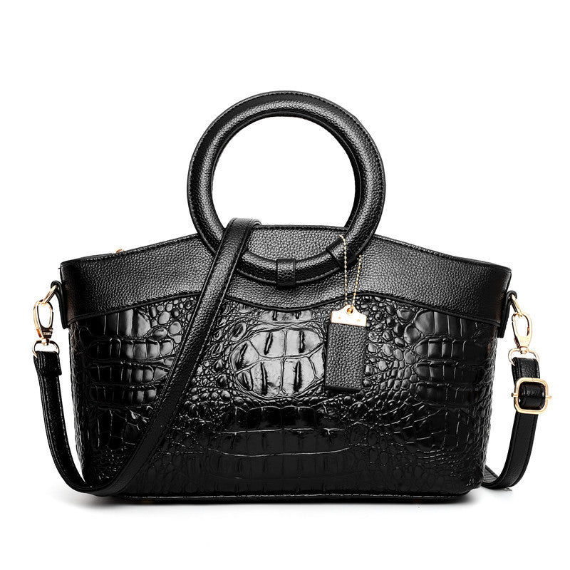 Black handbag with crocodile texture and round handles on a white background
