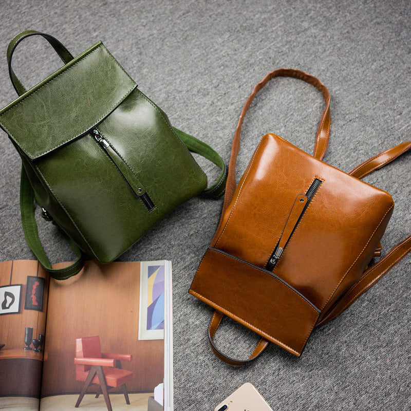 Green and brown leather backpacks on a gray surface with an open magazine.