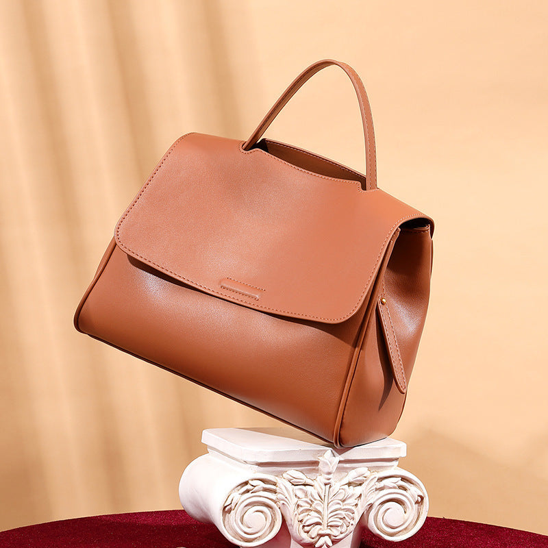Brown leather handbag on a decorative white pedestal against a beige background