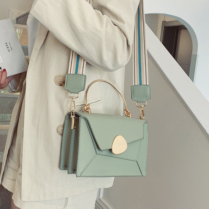 Light green handbag with gold accents held by a person wearing a beige coat.