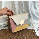Color-blocked handbag with a chain detail held by a hand against a white fabric background.