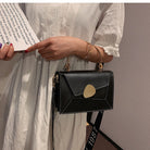 Person holding a black handbag with a gold clasp against a neutral background