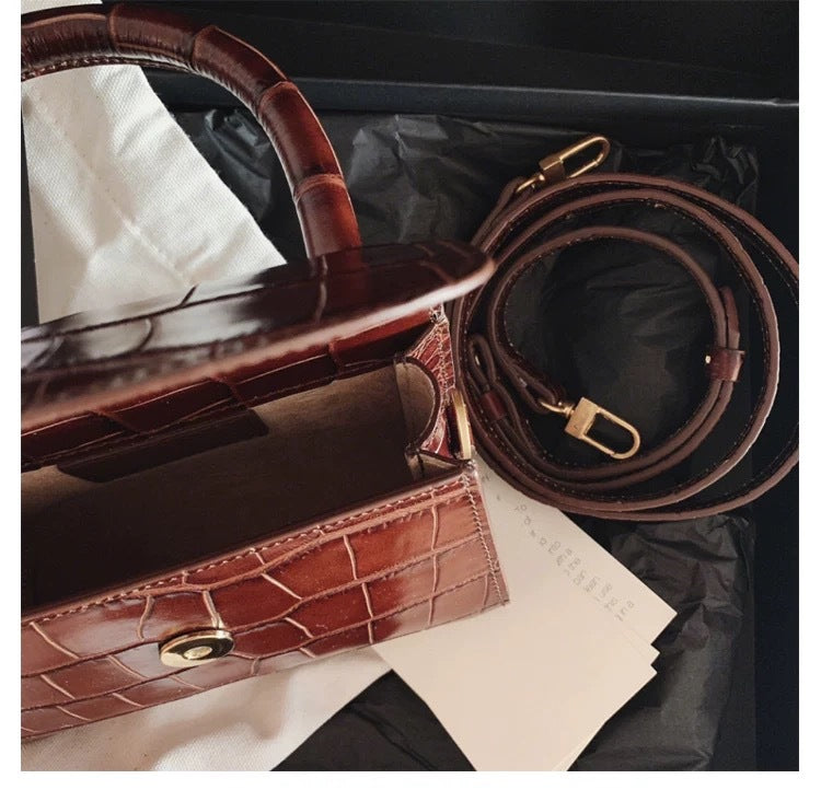 Brown crocodile skin handbag with gold hardware on a black surface