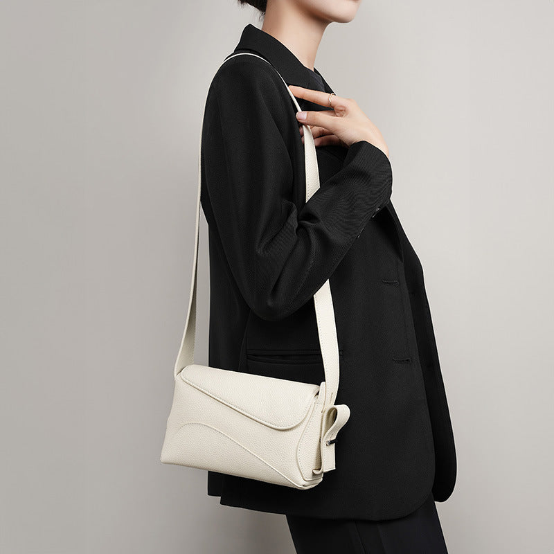 Person wearing a black outfit with a white crossbody bag against a plain background