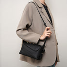 Person wearing a beige coat holding a black handbag against a plain background