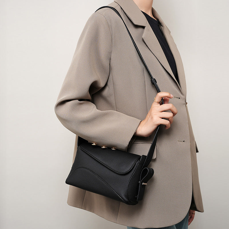Person wearing a beige coat holding a black handbag against a plain background