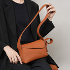 Person holding a brown leather handbag against a neutral background
