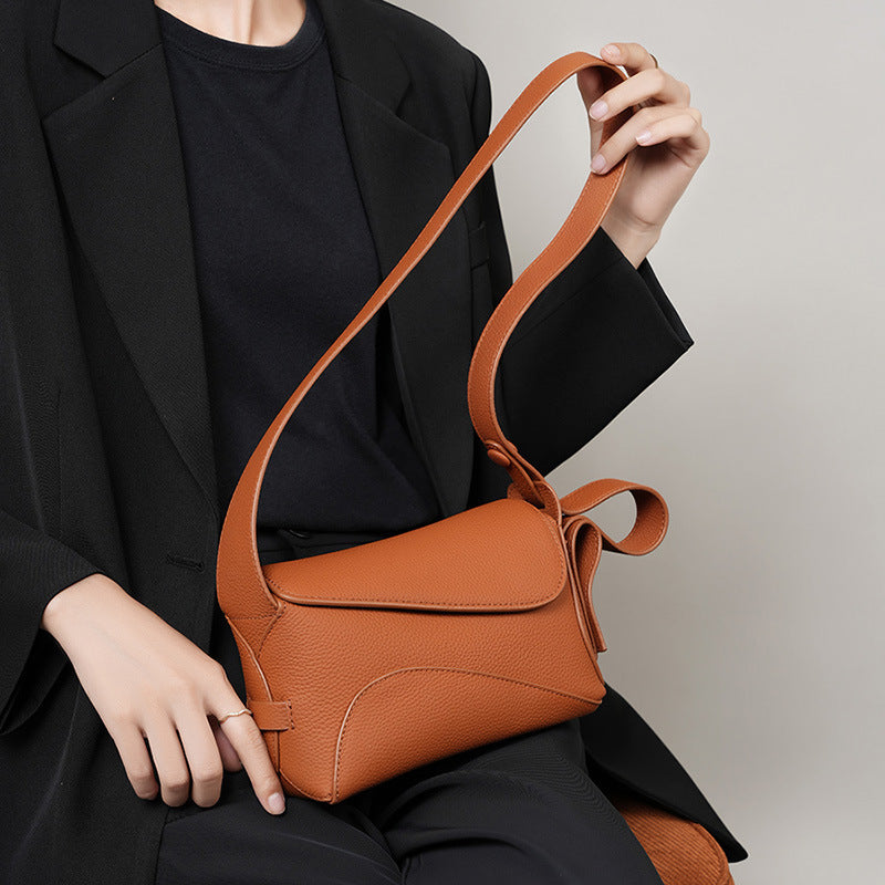 Person holding a brown leather handbag against a neutral background
