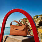 Brown leather handbag on a stone ledge with a red arch and ocean view