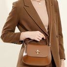 Person wearing a brown coat holding a matching brown handbag against a neutral background