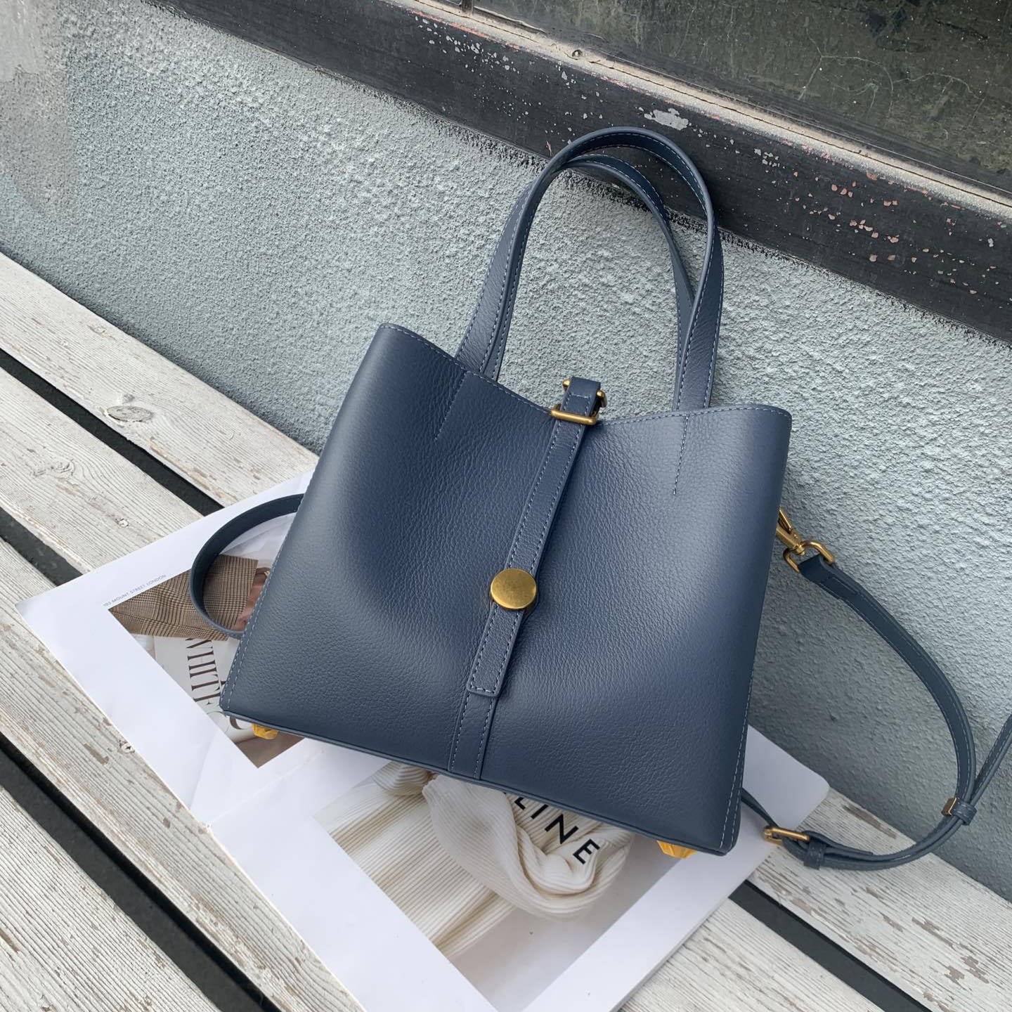 Blue handbag on a wooden surface with a magazine underneath