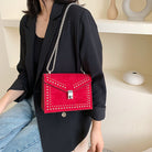 Person wearing a red studded handbag with a chain strap.