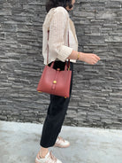 Person holding a red handbag against a stone wall.