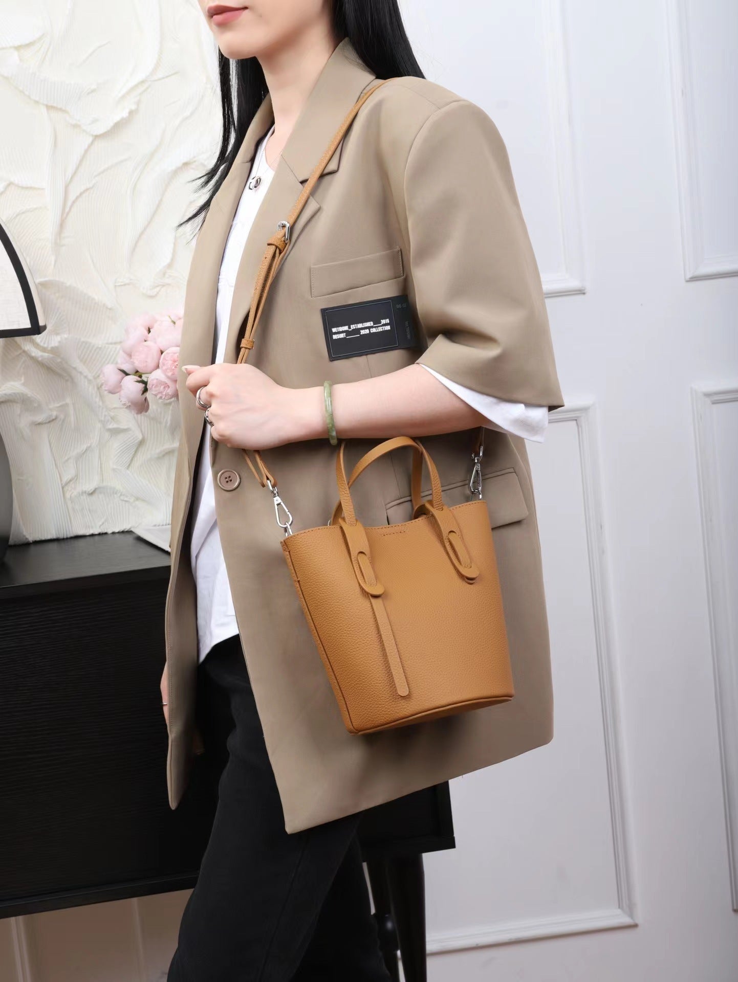 Woman holding a tan handbag against a neutral background