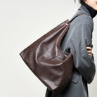 Person wearing a brown leather bag over their shoulder against a plain background