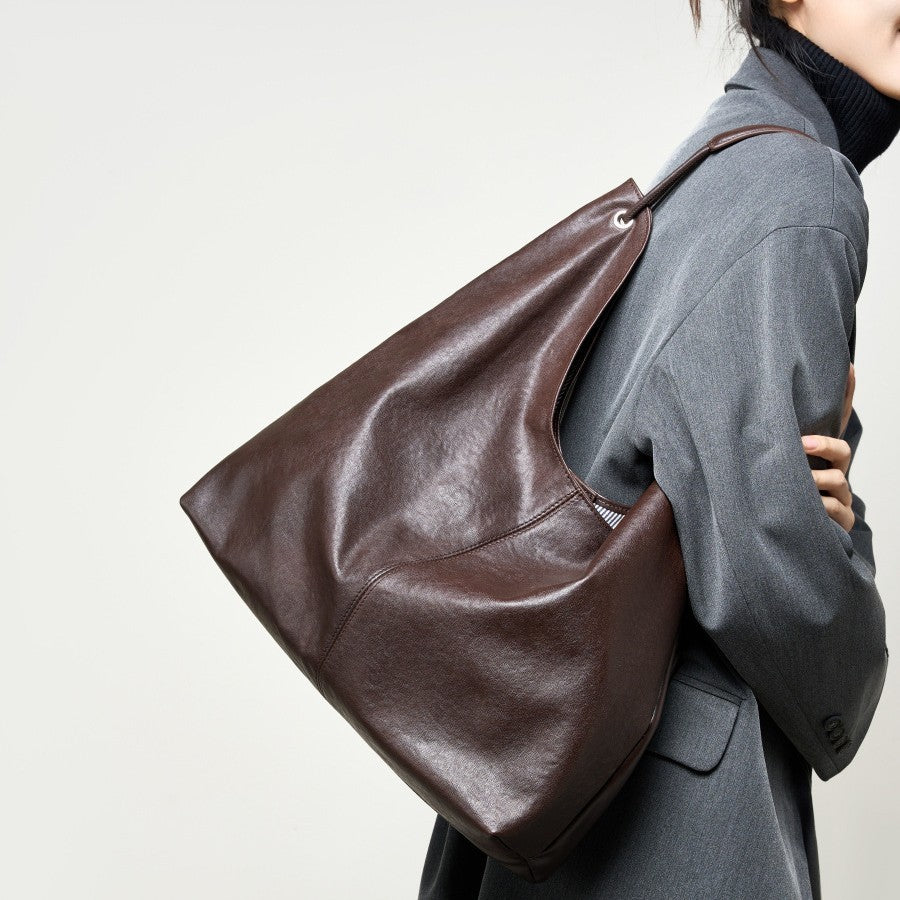 Person wearing a brown leather bag over their shoulder against a plain background