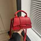 Red handbag held by a person in front of a window with blinds.