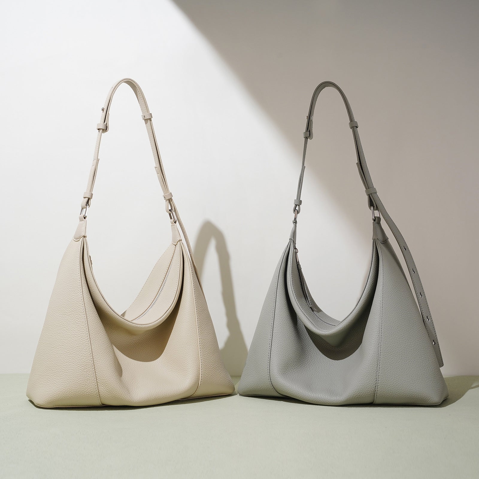 Two handbags, one beige and one gray, on a light background