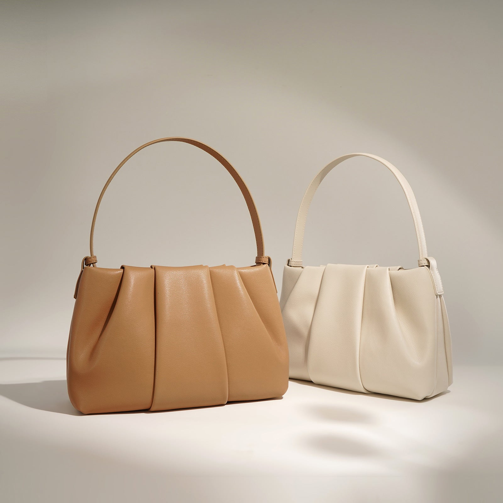 Two handbags, one brown and one beige, on a neutral background