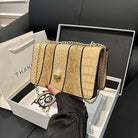 Beige crocodile-patterned handbag with gold chain held by a person, displayed in an open white box.