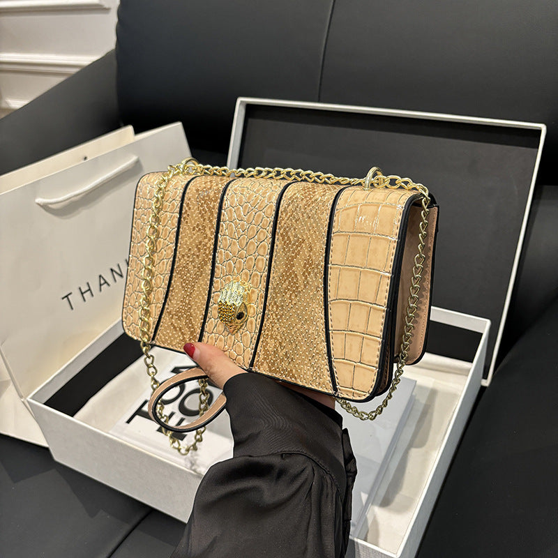 Beige crocodile-patterned handbag with gold chain held by a person, displayed in an open white box.